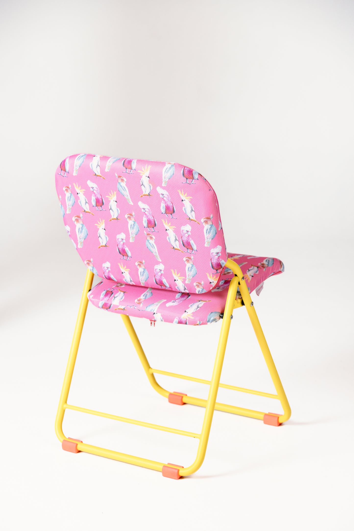 Pink folding chair with a colourful pattern on a white background with yellow frame