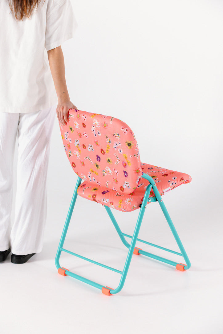 Person holding a pink chair with floral pattern with a green frame