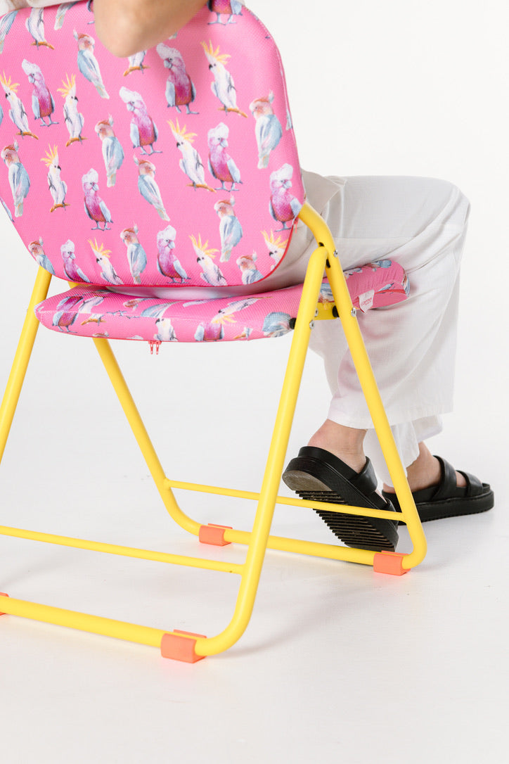 Person sitting on a yellow chair with a pink cushion featuring birds. 